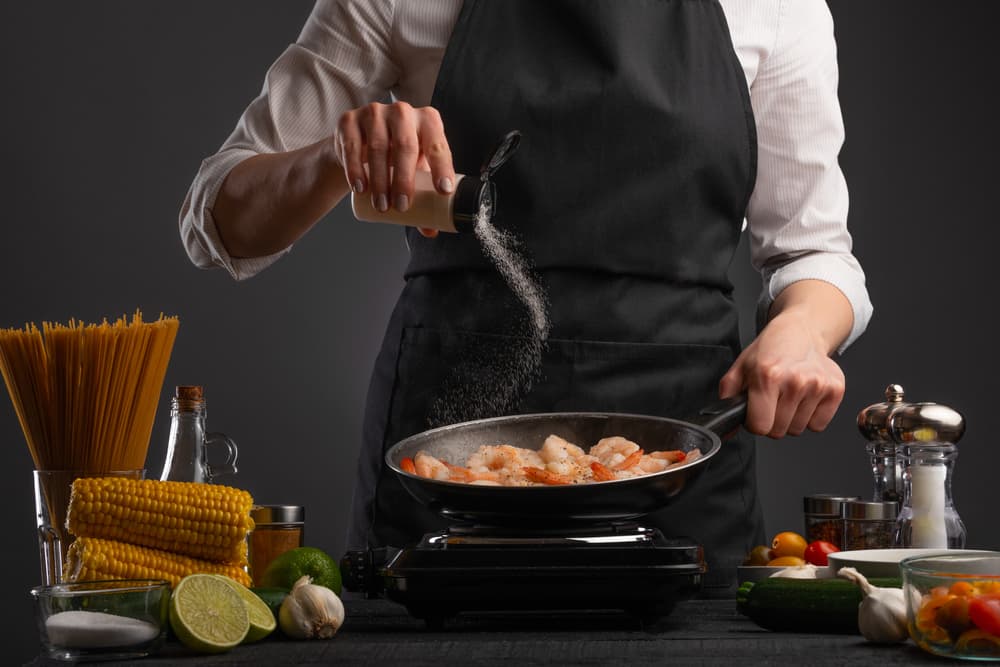 Chef cooking prawns in pan and adding salt